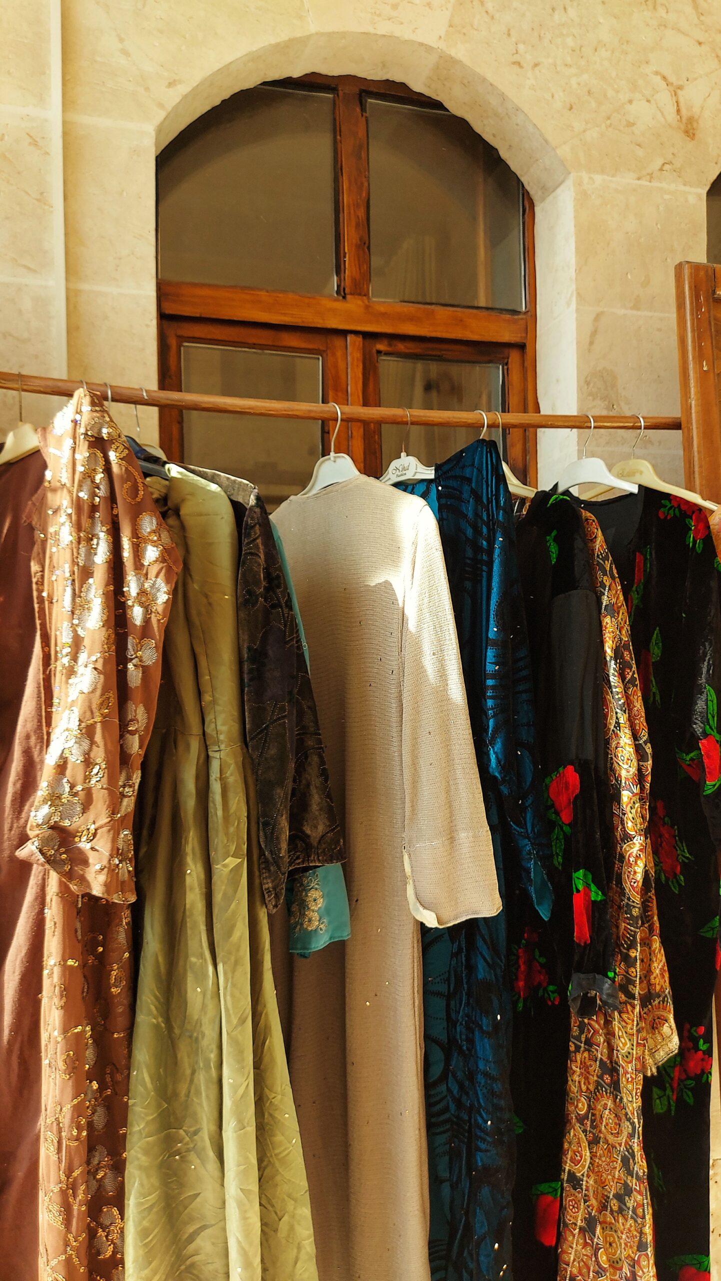 Assorted patterned women’s dresses and garments hanging on a wooden clothing rack in a rustic interior.